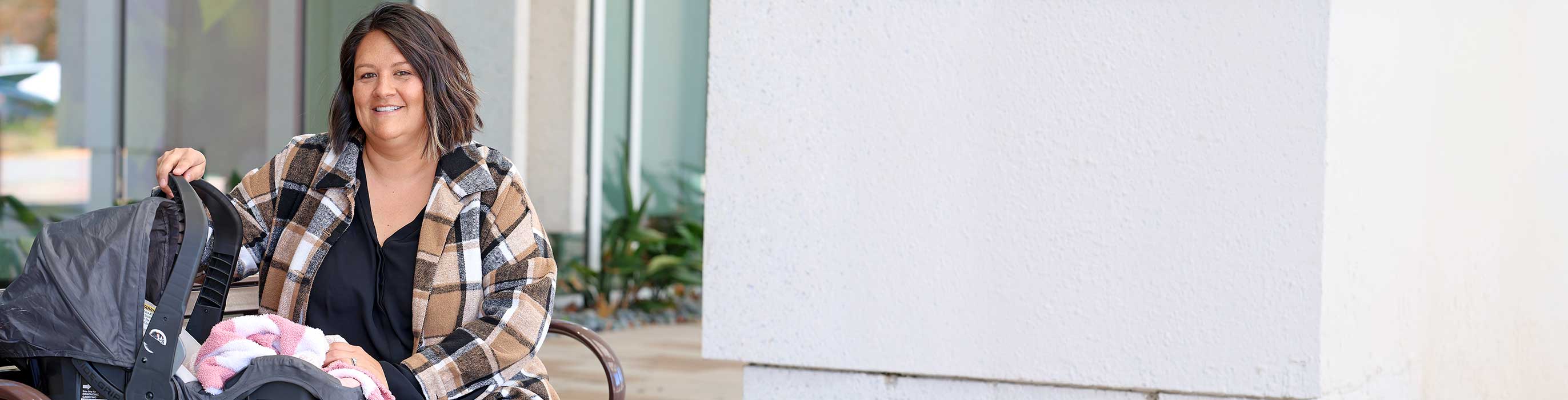 A smiling woman sitting on a bench with a stroller.